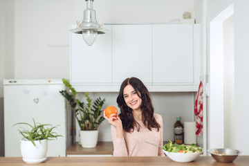 Smiling young woman in the kitchen near desk and holds a fruit in his hand. Healthy life concept