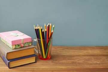 Color pencils, books and gift box on wooden background.