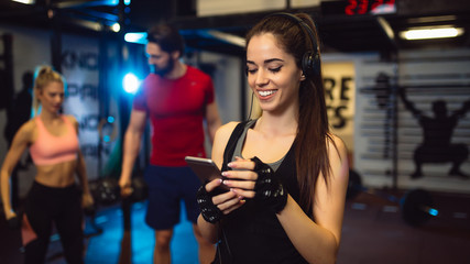 Portrait of young sportswoman with smartphone listening to music in gym.