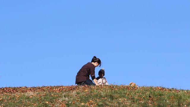 Lovely picture, cute baby and young mother play with autumn leaves, blue sky 
