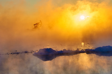 Obraz premium The oil sucking machines in the vapour lakeside sunrise.