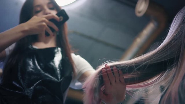 Hairdresser take a photo of woman's long coloured hair on smartphone in hair salon. Hairdresser admires her work and shows strands of dyed hair. Down angle. Slow mo