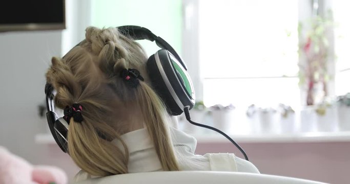 A little girl with ponytails and pigtails is listening to music on headphones.