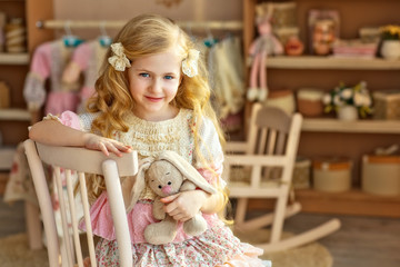 Romantic little girl with long blond hair in a beautiful pink vintage dress with a plush Bunny sits...