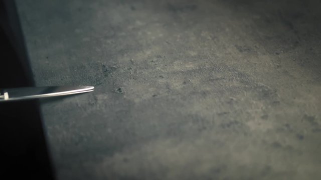 A pair of metal scissors lies on the table and a female's hand with lovely red manicure gently takes them. Closeup, slow mo