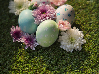 Beautiful hand painting Easter eggs, green, blue and white color painted Easter eggs with sweet pink and purple Spring flowers on green grass with sunrise or sunset light background