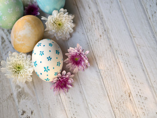 Obraz na płótnie Canvas Cute and beautiful hand painting Easter eggs with white, yellow, blue and green color egg shells and pink and white color Spring flowers on white vintage wooden table, top view
