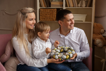 Mother, father and their son preparating for Easter day. Young family painting eggs in spring wreath