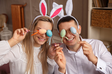 Funny couple wearing bunny ears and having fun with Easter eggs at Easter day. Friends playing hunt...