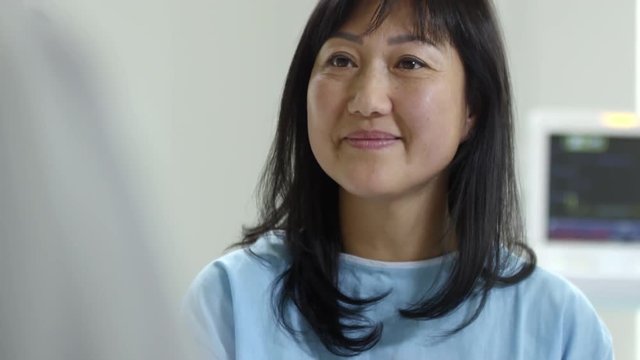 Tilt up of cheerful female patient in hospital gown nodding and listening to her doctor talking about successful treatment