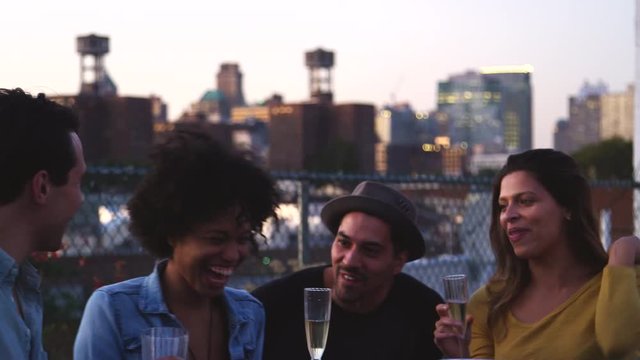 Happy friends talk and drink at a table on Brooklyn rooftop