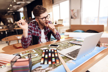 Freelancer man yawning at laptop sitting at desk.