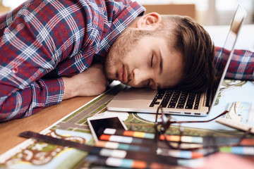 Freelancer man sleeping at laptop sitting at desk.