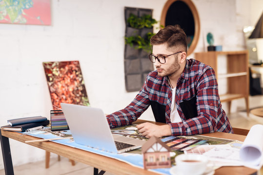 Freelancer man looking at laptop sitting at desk.