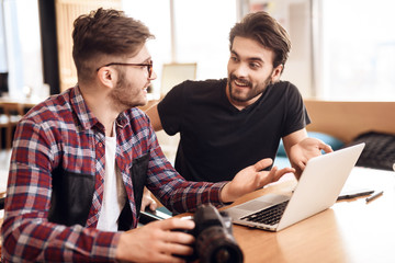 Two freelancer men looking at photos at laptop at desk.