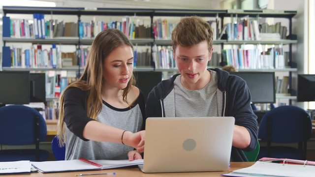Male And Female College Students Working On Laptop In Library