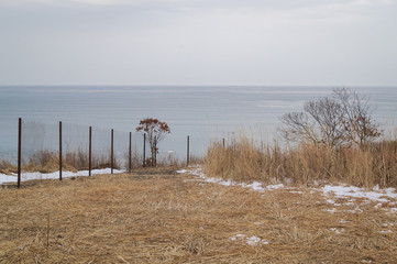 Fototapeta na wymiar Iron fence and autumn field on the background sea. Prohibited access to the public beach.