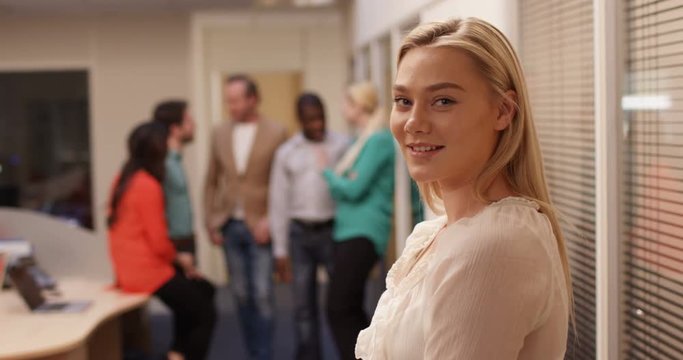 4K Successful young businesswoman smiling to camera with her team chatting in the background. Slow motion.