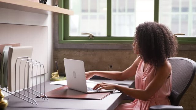 Young black woman working alone with laptop in small office