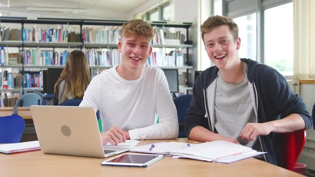Two Male College Students Working On Laptop Together In Library