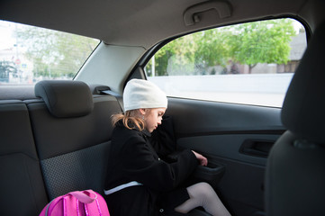 sad little girl in coat and hat sitting with a backpack in the car