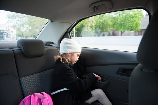 Sad Little Girl In Coat And Hat Sitting With A Backpack In The Car