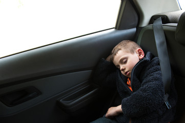 sleeping little kid sitting in car in back seat with seat belt