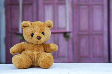 The Lonely teddy bear sits in front of a pink wooden background