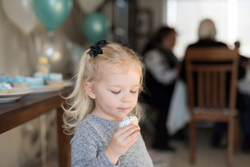 little girl holding a cupcake with icing on face at family birthday party