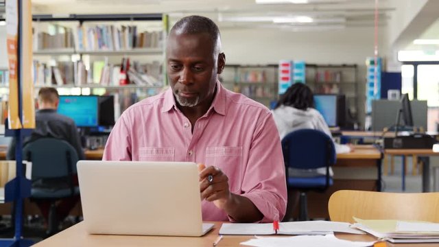 Mature Male Student Working On Laptop In College Library