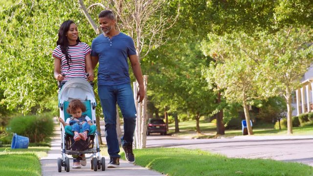 Couple Push Daughter In Stroller As They Walk Along Street