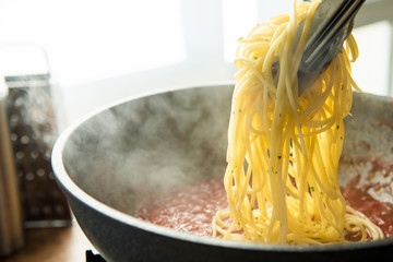 spaghetti being put into hot bolognese sauce in the pan