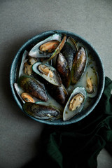Kiwi mussels cooked in marinier sauce with white wine and parsley in hand-crafted blue ceramic plate on gray background