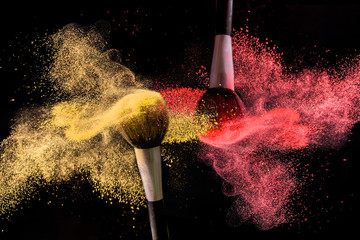  Two brushes for makeup with gold and red make-up shadows in motion on a black background.