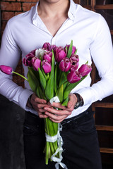 Grand bouquet of tulips, spring flowers in the hands of a sports guy in a white shirt. Festive bouquet for mother's day