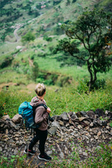 Fototapeta na wymiar Female hiker with backpack walking down cobbled path to the lush green Paul valley. Santo Antao Cape Verde. Cabo Verde