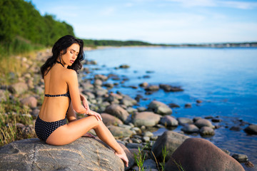 Obraz premium back view of beautiful girl in swimsuit sunbathing on rocky beach