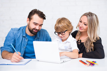 parents helping to happy cute little school boy doing homework and using laptop