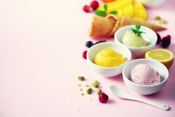 Red, pink, yellow, green, white ice cream balls in bowls, waffle cones, berries, orange, mango, lemon, mint, pistachio, pink shabby chic background. Ice-cream colorful collection, summer concept