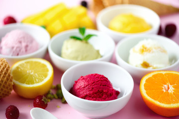 Red, pink, yellow, green, white ice cream balls in bowls, waffle cones, berries, orange, mango, lemon, mint, pistachio, pink shabby chic background. Ice-cream colorful collection, summer concept