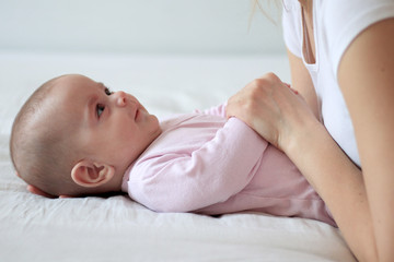 Mother playing with baby daughter on a white bed