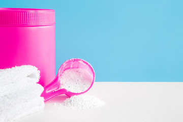Pink bottle, powder and white towels on the blue background. Detergent for clothes washing. Dry cleaning concept. Clothes care. Chores of housewife. Regular washing. Empty place for text. Front view.