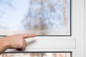 Man's hand pointing to the window glass humidity. Room airing problem.