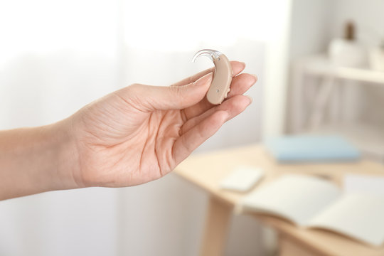 Woman holding hearing aid on blurred background, closeup