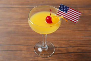 Glass with alcoholic cocktail and small American flag on table