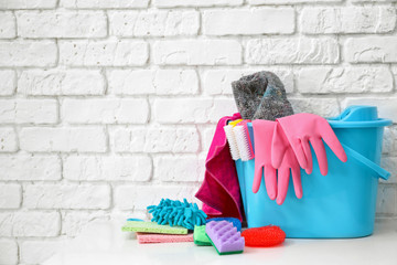 Bucket with cleaning supplies and tools on table near brick wall