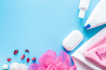 White shower bottles, soap, towels with pink wisp on the blue background. Body relax and care products for women. Empty place for text or logo. Top view.