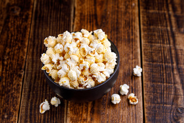 A bowl with seductive popcorn on a wooden background.