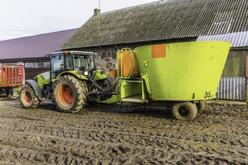 Obraz premium Tractor with a trailer on an agricultural farm. Distributor of mixed fodders for cows. Late fall. Podlasie, Poland.