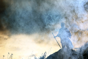 Silhouette of a warrior with a sword in the smoke of a mountain war